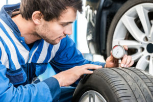 young male auto body technician pressing gauge into tire for proper tire care