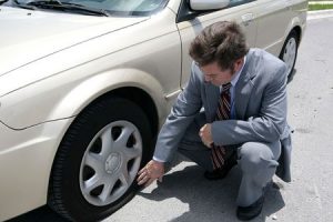 A man dressed for a business meeting discovering a flat tire on his car