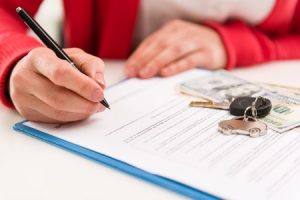 Closeup of woman auto dealer signing rental contract in the office. Car key and money on papers.