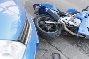 The motorcycle crashed into the bumper of the car on the road. The motorcycle lies on the road near the car.