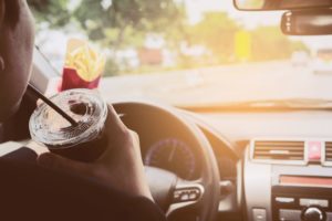 Man driving car while eating French fries and soft drink with potential for car accident