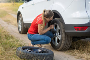 young woman changing flat tire doing roadside assistance herself.